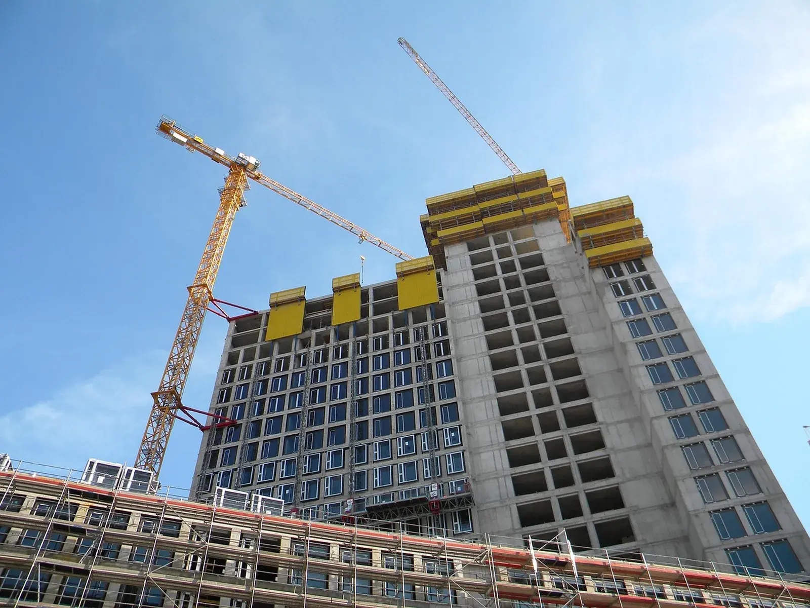 A reinforced concrete tower under construction with tower cranes over the topmost floor